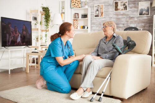 Young female nurse wearing blue uniform talking with senior woman in nursing home.